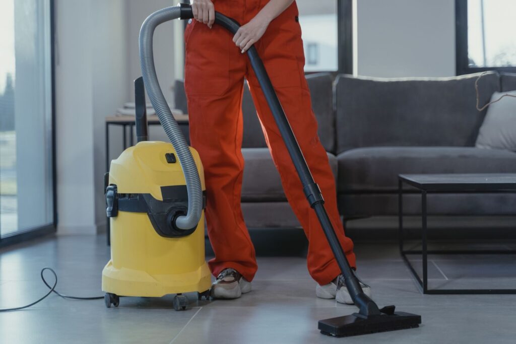 Agent d’entretien en tenue orange passant l’aspirateur dans un salon moderne