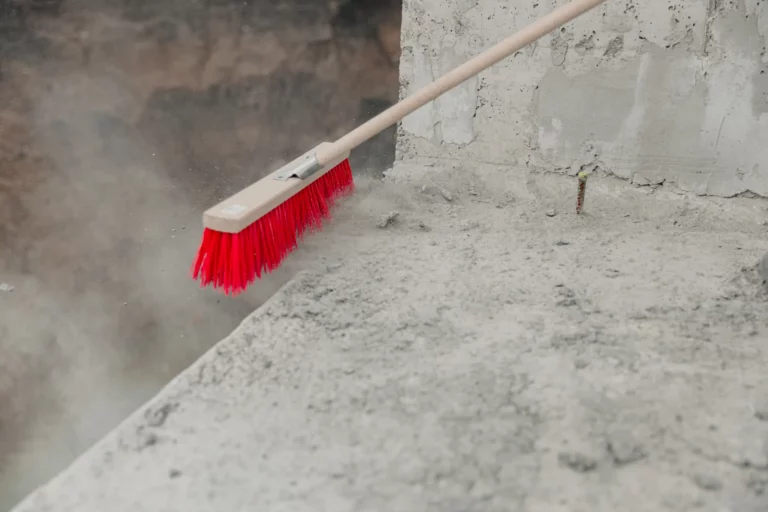 Balai à poils rouges poussant la poussière de béton après des travaux
